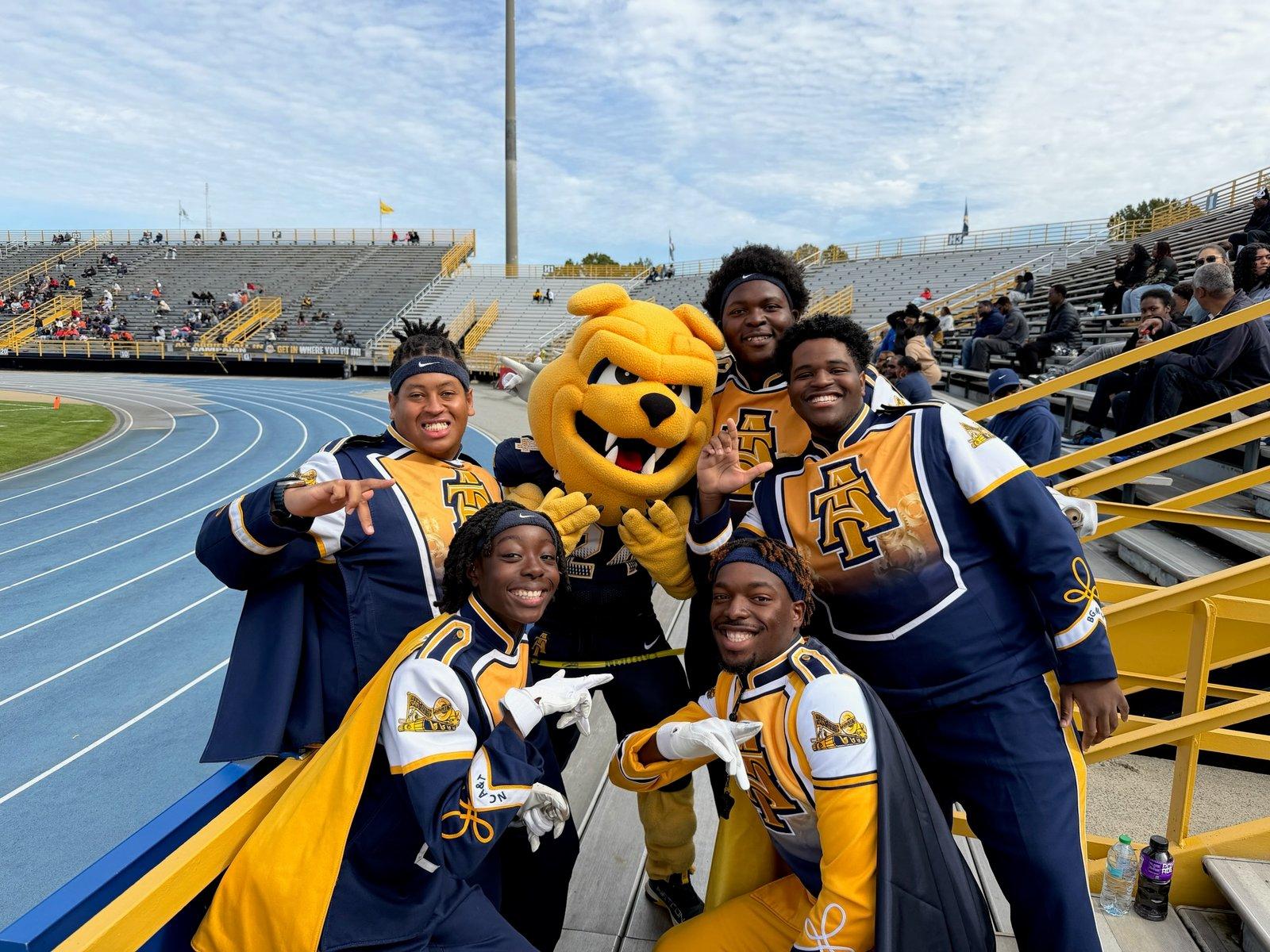 Blue and Gold Marching Machine members in uniform with the N.C. A&T mascot at a football game